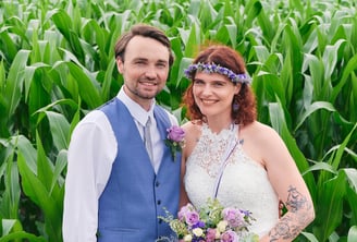 a bride holding a bouquet and a groom standing next to each other in a corn field