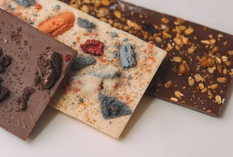 3 overlapping chocolate bars with toppings. Milk, white, & dark chocolate with colorful macaroon nut