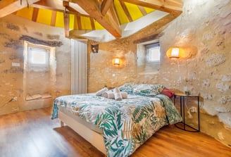 Chambre du moulin vue en grand angle, deux fenêtres, serviettes et éclairage mural mis en valeur