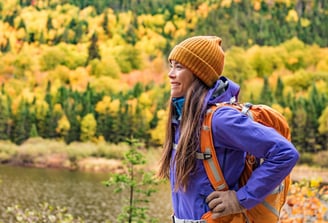Happy lady sideways with orange backpack and yellow trees in the background