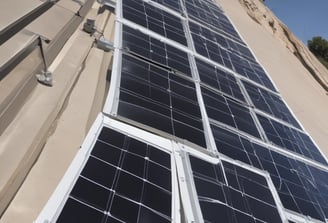 A field of solar panels is positioned under a clear blue sky. The panels are arranged in rows, capturing sunlight efficiently. The sleek, reflective surface of the panels gives a modern and clean look.