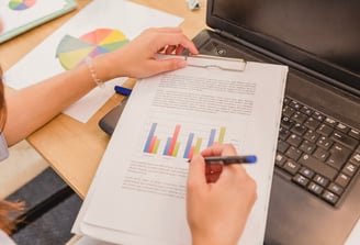 Personne annotant un document imprimé avec des graphiques à côté d'un ordinateur portable.