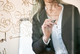 Personne écrivant des formules sur une vitre transparente.