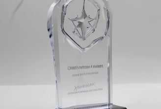 A spacious, well-lit industrial setting with numerous large white machines lined up in parallel rows. A person in uniform appears to be operating one of the machines. Red and blue bins are placed at intervals along the line of machines, which appear to be automated textile machines. The facility is clean and modern, with the floor marked with geometric patterns.