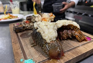 a lobster tail on a cutting board with a chef in the background