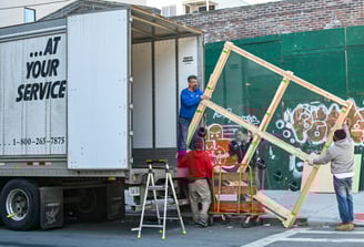 Four people lifting a large window out of a moving truck