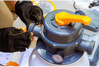 Image of a pool tech with gloves on inspecting a pool filtration system
