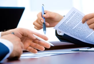 Hands hovering over a desk holding a pen and document