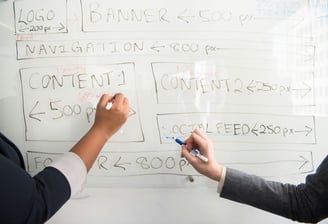 Two team members are planning the layout of a website on a whiteboard 