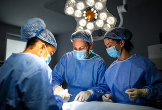 Three surgeons in blue scrubs and masks are focused on operation in operating room.