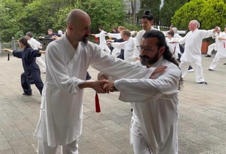 Ismet Himmet guiding Mehmet Başkak during a Tai Ji form correction at an outdoor group training.