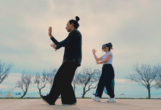 Ebru Tütek and student practicing Bagua walking by the sea, with bare trees and ships in the distance.