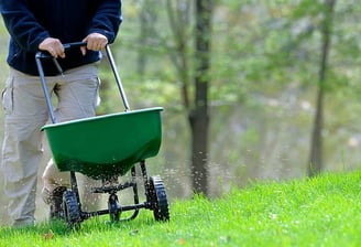 a man is walking in the grass with a lawn spreader