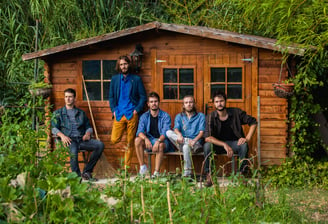 photographie d'un groupe de musiciens de rock devant un cabanon de jardin en pleine nature