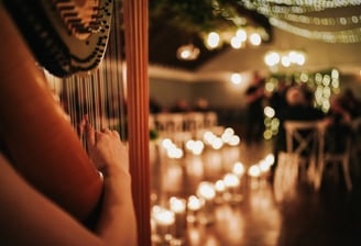 Wedding ceremony with room lit by numerous candles. Harp being performed is focus of the picture.