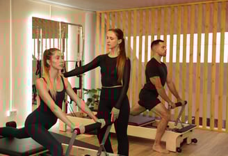 Pilates instructor guiding a student on a duo reformer, while another person exercises in the back