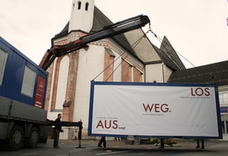 Kran bei der Aufstellung des Ausstellungscontainers "Aus weg los!" auf einem Dorfplatz.