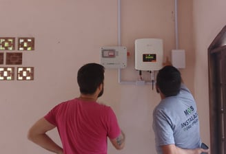 Técnicos em energia solar em frente a display digital de monitoramento fotovoltaico na parede