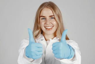 Female in lab coat with blue gloves giving thumbs up sign