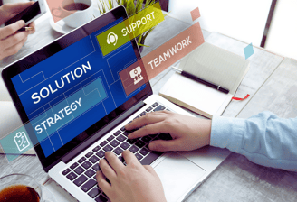 Two consultants work at a desk, focusing on one typing on a laptop with the screen displaying "Solution," faces unseen.