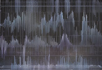A person is seated in a professional recording studio, surrounded by various electronic equipment including a computer, multiple speakers, and audio mixers. The room is dimly lit, creating a focused and immersive atmosphere. The walls are lined with acoustic panels to optimize sound quality.