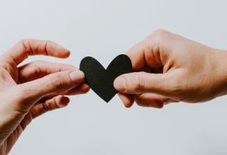 Hands Coming together both holding onto a heart shaped piece of black card
