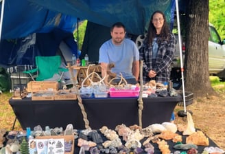a man and woman standing in front of a vendor table with a variety of rocks and antlers