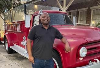 Photo of attractive dark skinned male leaning against a vintage red fire truck