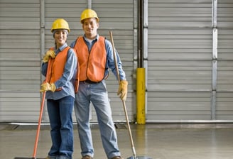 a man and woman in safety vests and hard hats cleaning warehouse