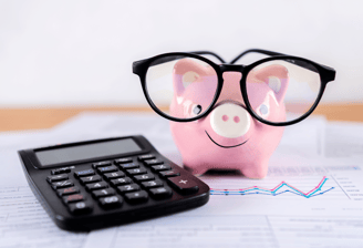 piggy bank holding glasses on financial paperwork next to a calculator