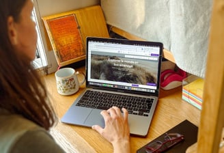 a woman sitting at a desk with a laptop and a cell phone
