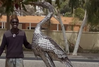 Moussa Fofana posant avec une sculpture métallique d’un héron géant fabriqué à Dakar