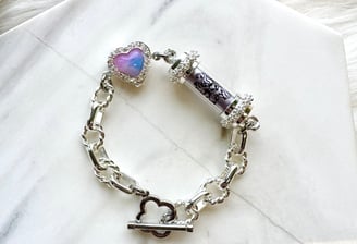 Features a silver chain with larger, oval links. It has a central cylindrical element with a dark pa