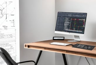 Stanowisko pracy z rysunkiem technicznym w tle oraz komputerem z AutoCADem