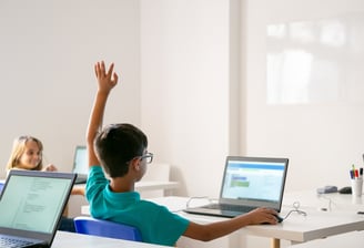 Children raising hands and engaging in a tech learning environment with laptops