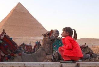 Petite fille fait un bisous au chameau devant les pyramides de Gizeh