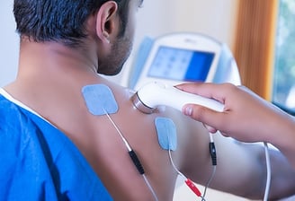 Electrotherapy treatment on session at home for shoulder pain relief using physiotherapy equipment.