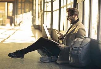 a man sitting on a suitcase and looking at his laptop