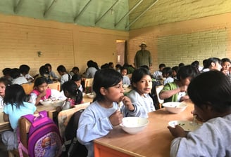 a group of children eating food in a classroom