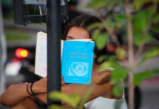 Uma pessoa lendo um livro de capa azul onde o livro tampa seu rosto