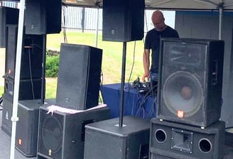 man outdoors under a tent standing behind speakers