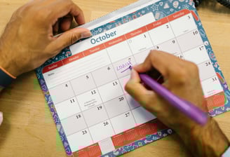 a person holding a pen and writing on a calendar