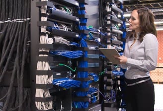 mulher em ambiente datacenter observando servidores e nobreaks