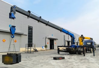 Blue SQS250G-5 10-ton truck mounted (lorry) crane undergoing load test in factory yard. Extended boom, test weight on hook.