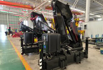 Factory floor view of several black SQZ132A.3 knuckle boom units, a type of crane machine, awaiting final