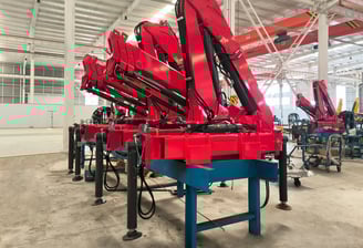 Production line: Red SQZ68B.3 (3.2T) articulating knuckle boom cranes on blue stands, pre-vehicle mounting.