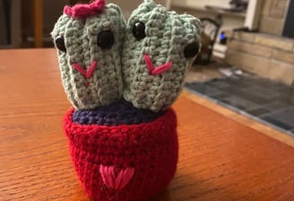 Small crocheted plush toy of two smiling cactuses sewed together and in a crocheted plant pot.