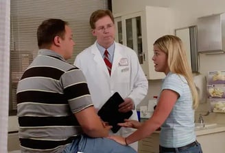 A doctor converses with a man and woman in a hospital setting, discussing medical concerns.