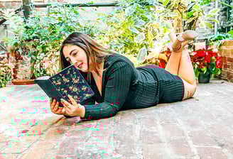 Patricia laying on the floor in a garden reading a journal