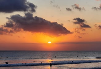 a sunset over kuta beach with people surfing